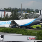 An image taken of the Amazon Cargo plane after the incident. The side of the plane is visibly damaged and emergency response vehicles can be seen in the background.