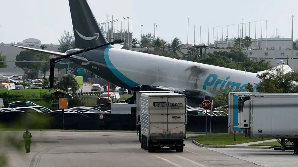 An image of the tail end of the Amazon Air cargo plane, dark scorch marks can be seen marking the side of the plane. The tail of the plane is slightly elevated into the air.