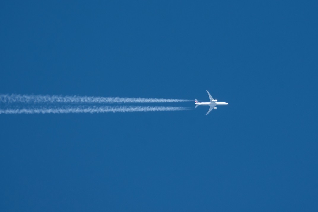 Photograph depicting an aircraft at altitude with contrails behind it as it flies above the clouds.