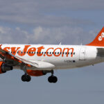 An easyJet aircraft mid-flight. The background is a blue, slightly cloudy sky.