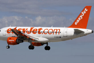An easyJet aircraft mid-flight. The background is a blue, slightly cloudy sky.