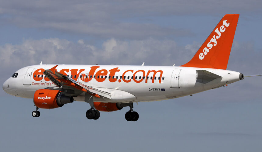 An easyJet aircraft mid-flight. The background is a blue, slightly cloudy sky.