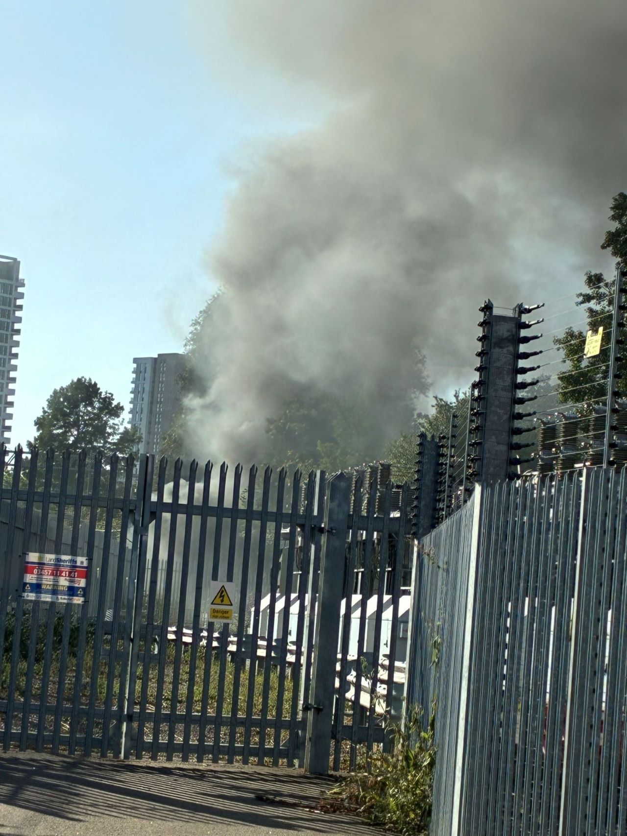 A plume of smoke from a fire beside the train track, which caused significant disruption to services in and out of London Paddington. The sky is clear and bright in contrast with the grey smoke erupting from the incident site.