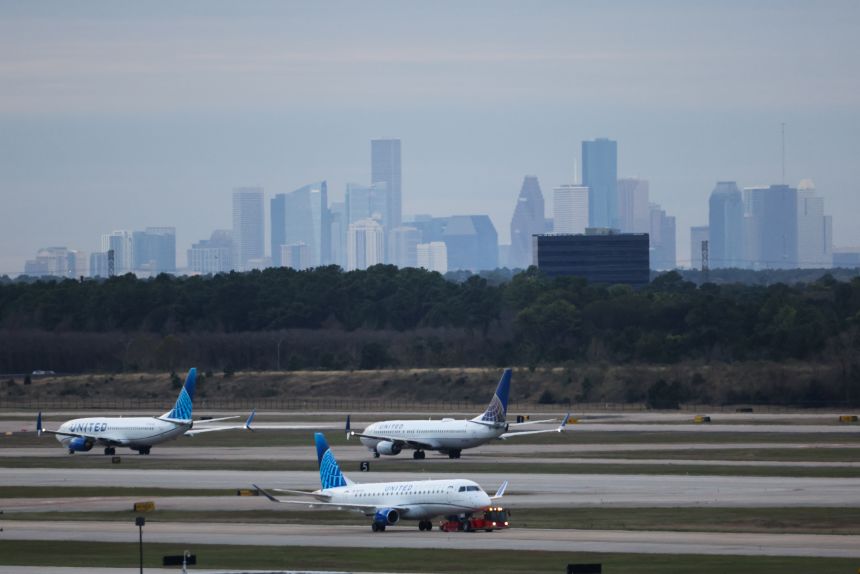 Three United Airlines planes on the George Bush Intercontinental Airport taxiway with city skyscrapers in the background under a cloudy sky.