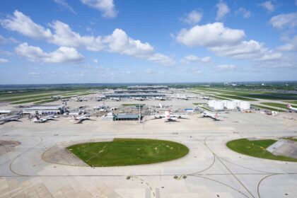 Image shows Heathrow Airport runways in the daytime with grass, aircraft and buildings visible