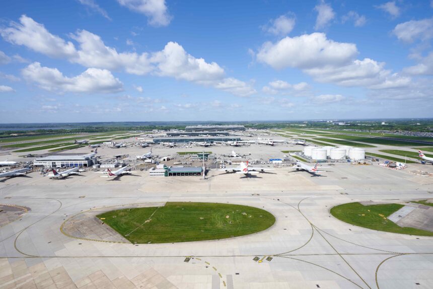 Image shows Heathrow Airport runways in the daytime with grass, aircraft and buildings visible