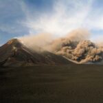 Huge volcanic ash cloud from Mount Etna falling down the mountain on the natural landscape.