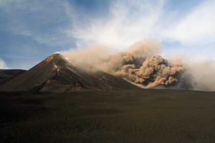 Huge volcanic ash cloud from Mount Etna falling down the mountain on the natural landscape.