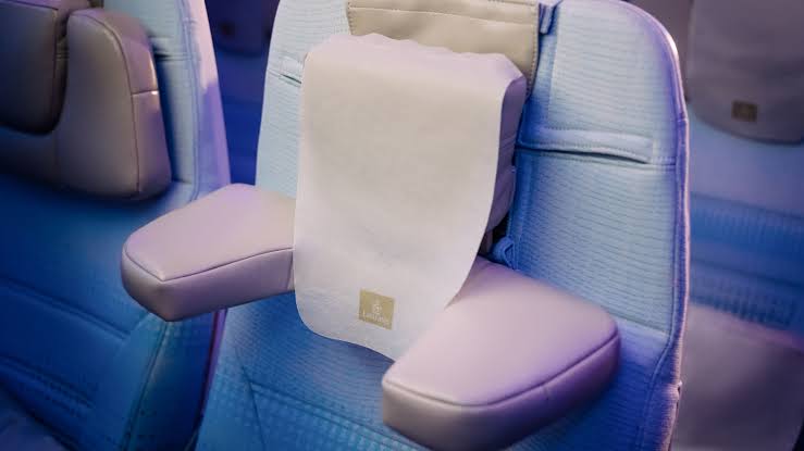 Close-up of an Emirates airplane seat featuring an adjustable headrest with padded side wings and a white fabric headrest cover.