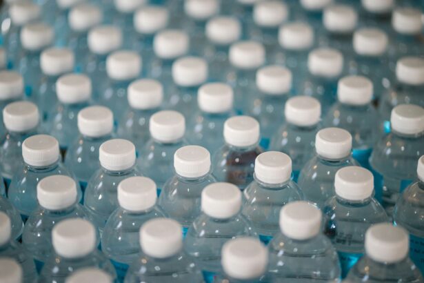 Numerous plastic water bottles are pictured line sup in rows. the image is taken zoomed in/close up from above at slight angle, so they appear in diagonal rows. The bottles become increasingly more stylistically blurred. The bottles are clear with white lids.