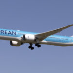 A Korean Air aircraft mid-flight, with a blue sky as the background.