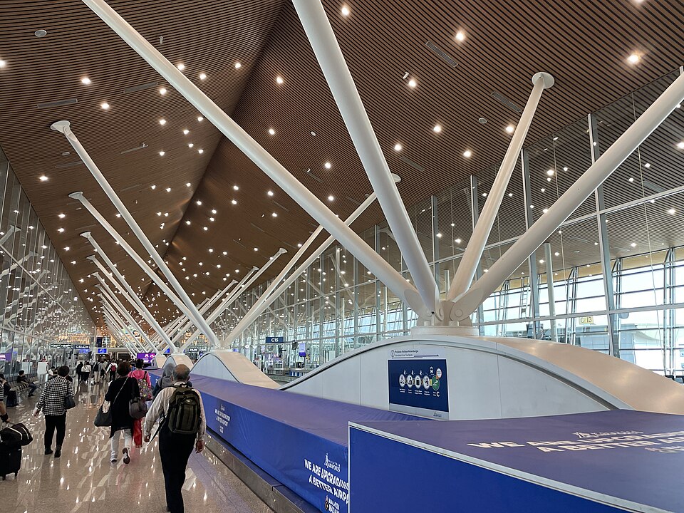 An image from the terminal of Kuala Lumpur International Airport showing passengers walking away from the camera down the terminal. There is a large divider in the middle of the terminal.