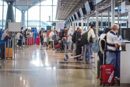 The image shows people in a long queue waiting to be seen at the several security desks at the side of the image.