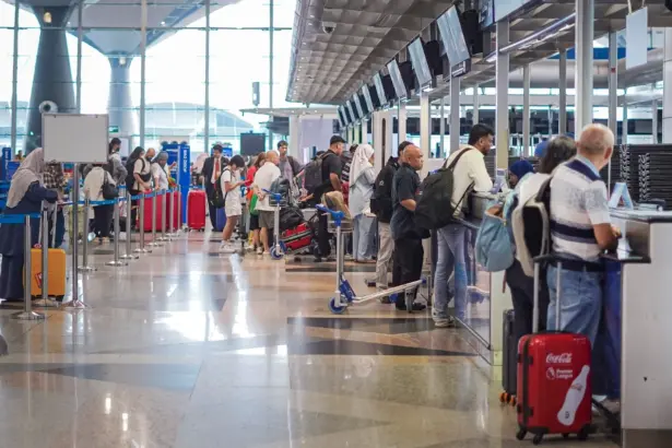 The image shows people in a long queue waiting to be seen at the several security desks at the side of the image.