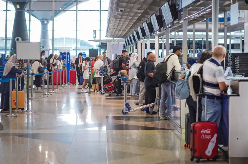 The image shows people in a long queue waiting to be seen at the several security desks at the side of the image.