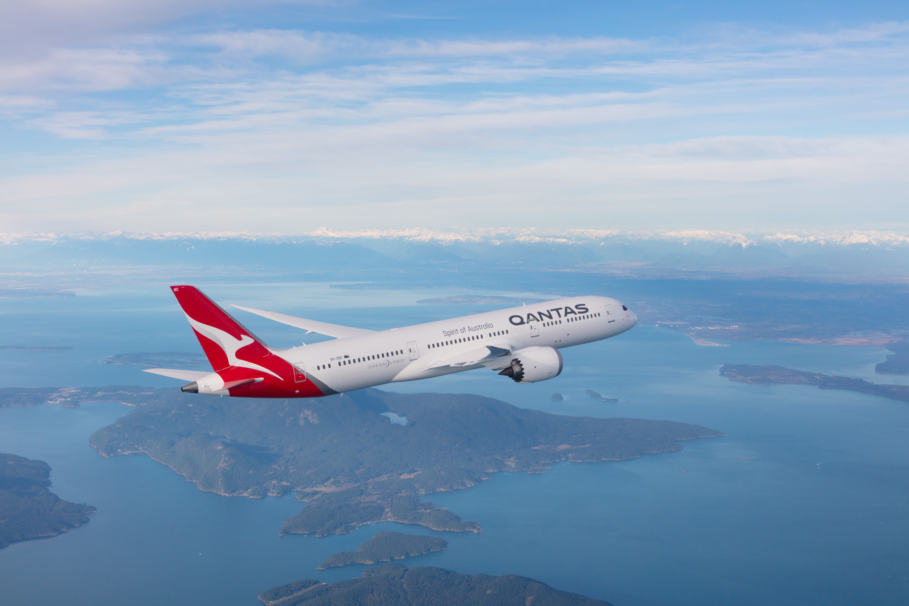A Qantas airplane soaring above the ocean, with clear blue skies and gentle waves below.