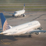 Two United Express commercial airplanes on an airport runway, one seen in the foreground in profile and the other in the background from the front.