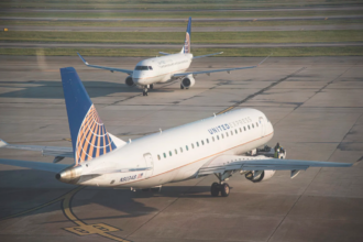 Two United Express commercial airplanes on an airport runway, one seen in the foreground in profile and the other in the background from the front.