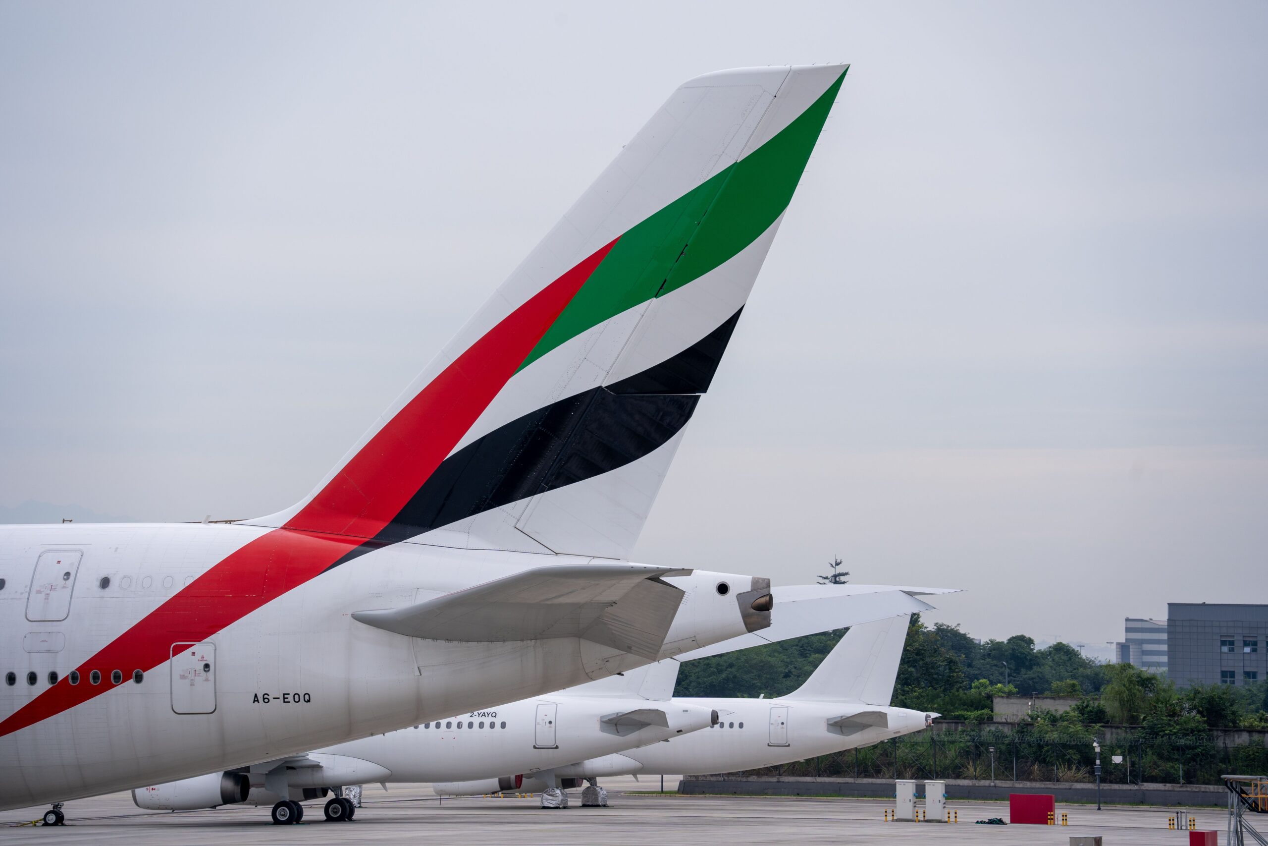 Close-up of the tail fin of an Emirates airplane painted with the United Arab Emirates flag colors, parked on an airport tarmac.