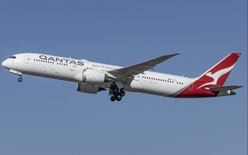 The photo shows a Qantas aircraft mid-flight, with a blue sky as the background.