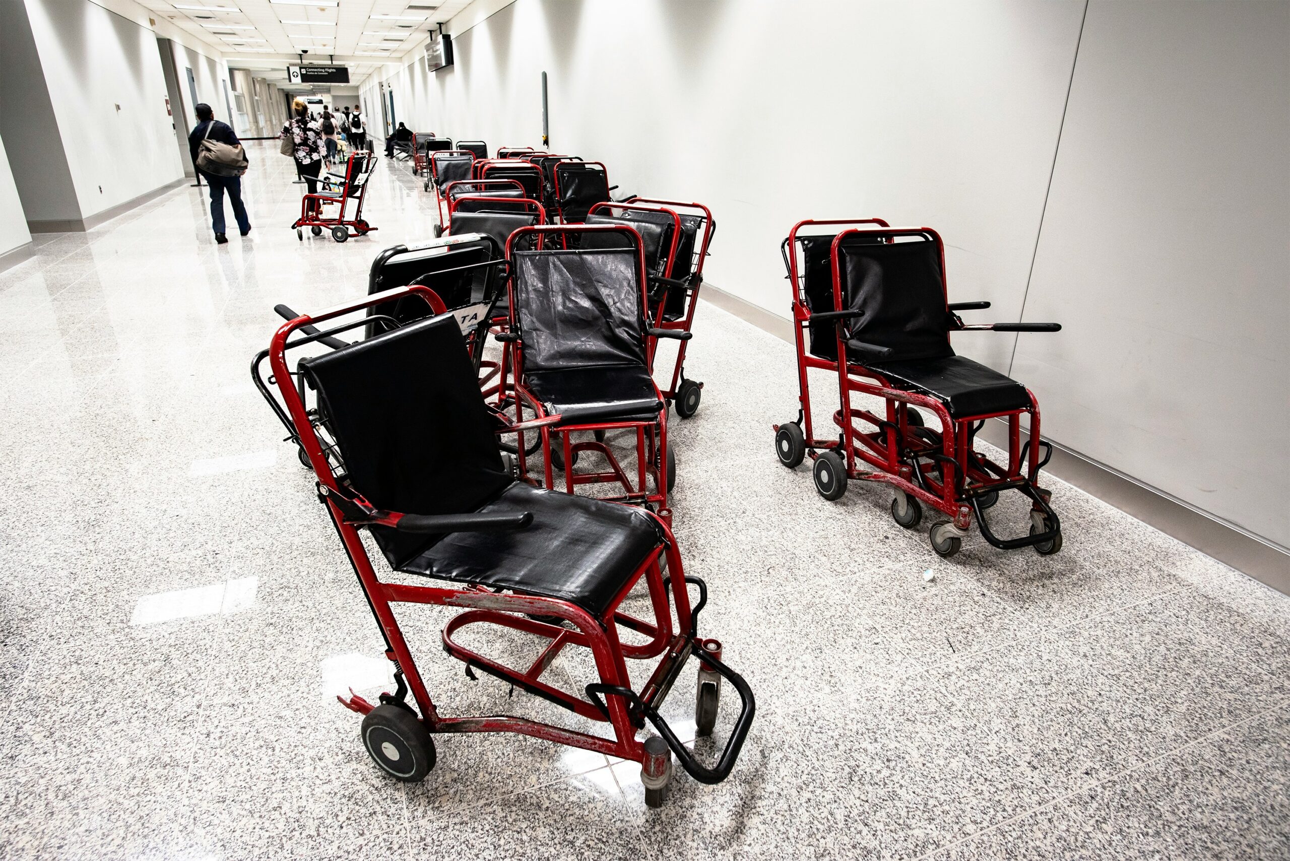 Several red-and-black wheelchairs lined up in an airport corridor