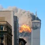 The image shows the moment the World Trade Center in New York City was hit by a hijacked plane during 9/11. Fire and smoke can be seen coming from the tall, sky-scraper building.