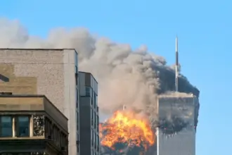 The image shows the moment the World Trade Center in New York City was hit by a hijacked plane during 9/11. Fire and smoke can be seen coming from the tall, sky-scraper building.