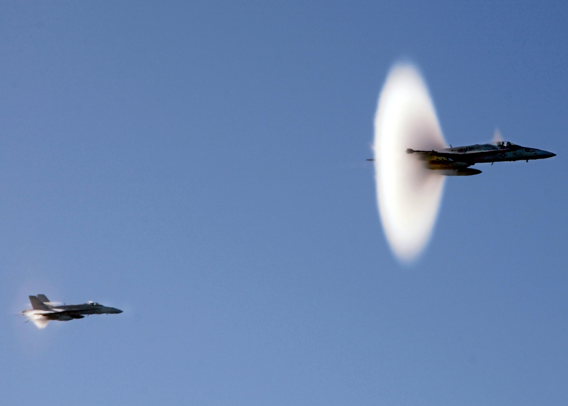 Image shows two military jets visibly breaking the sound barrier with a vapor cone.