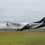 Air New Zealand aircraft on a runway with a green grass field and cloudy skies