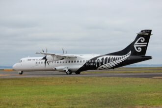 Air New Zealand aircraft on a runway with a green grass field and cloudy skies
