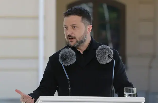 An image of Ukrainian President Volodymyr Zelensky giving an address with two microphones positioned in front of his face.