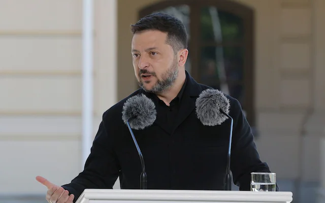 An image of Ukrainian President Volodymyr Zelensky giving an address with two microphones positioned in front of his face.