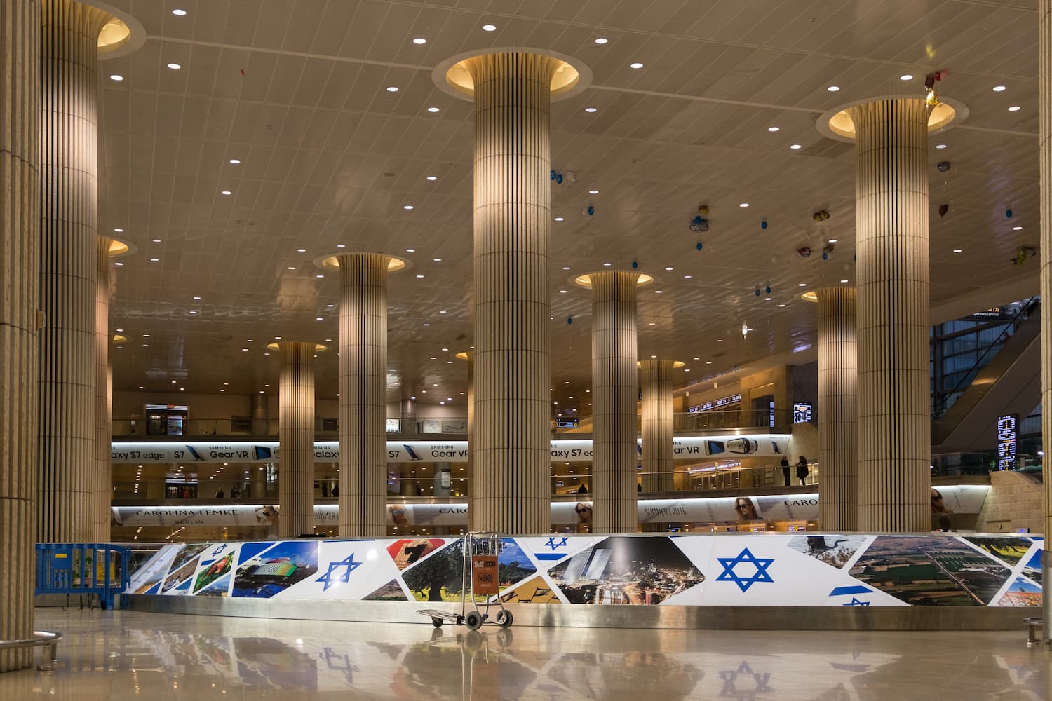 Image shows Ben Gurion Airport inside the terminal. There are tall pillars and advertisement boards. 