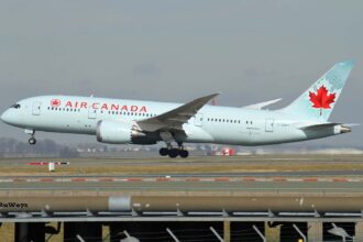 Air Canada Boeing 787-8 Dreamliner taking off, nose wheel raised, with a red maple leaf on a pale turquoise tail, seen above a fence and runway.