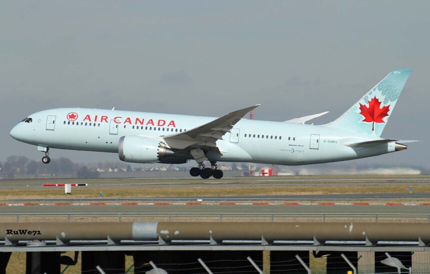Air Canada Boeing 787-8 Dreamliner taking off, nose wheel raised, with a red maple leaf on a pale turquoise tail, seen above a fence and runway.