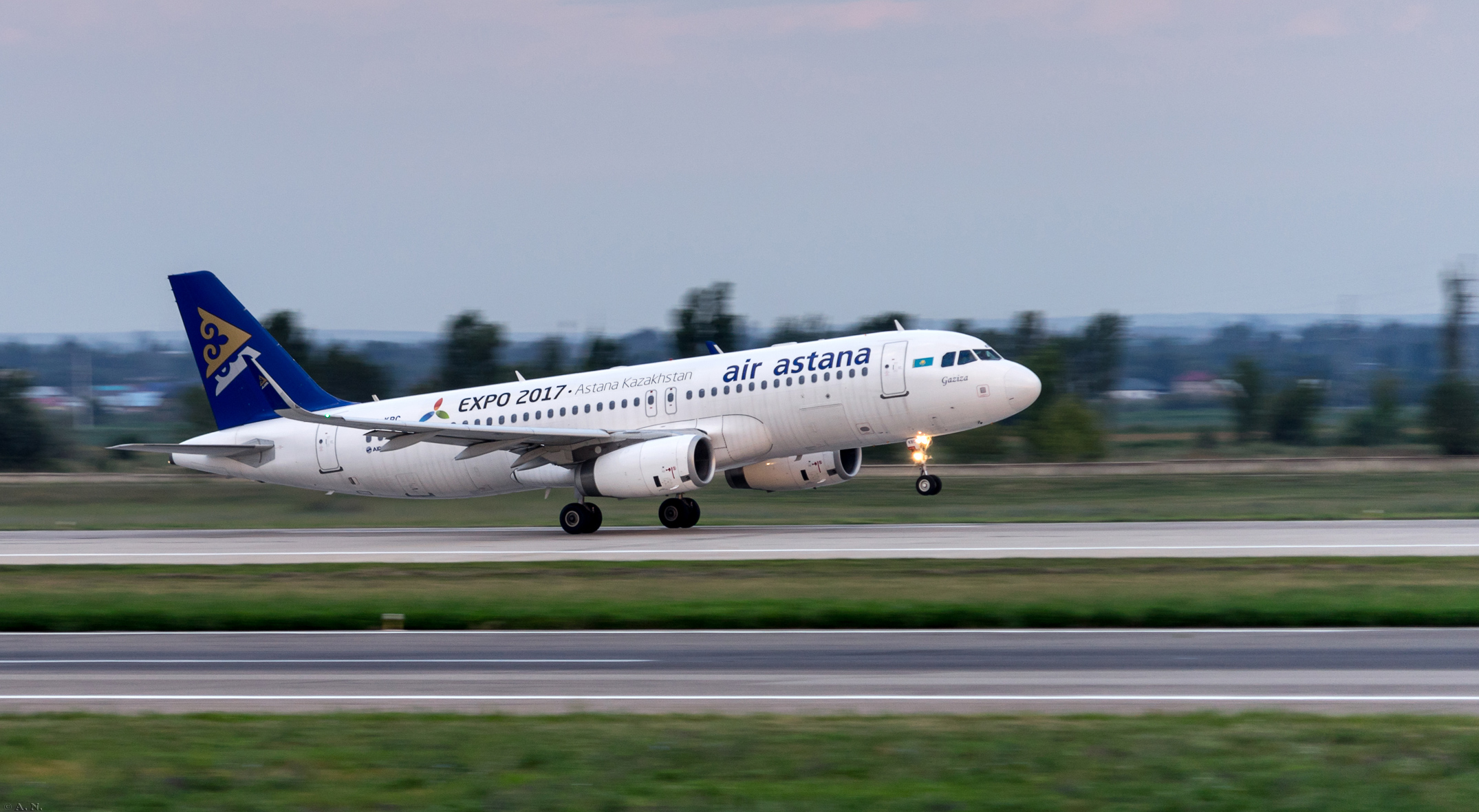 Air Astana Airbus A320 lifting off at dusk, nose wheel just airborne, landing lights on.