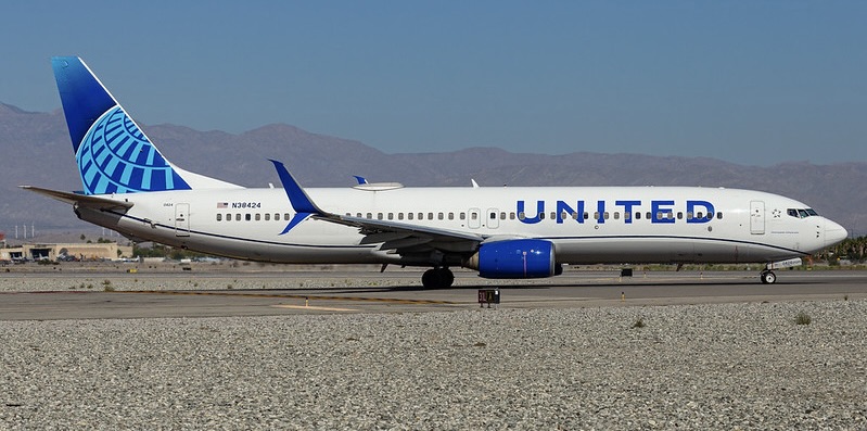 United Airlines Boeing 737-800 taxiing on a runway, with a blue globe design on the tail, blue engines and desert mountains behind a gravel foreground.
