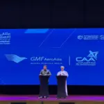 Photo of a presentation between President of Oman's CAA and AeroAsia's CEO (right to left) with a large board behind titled "GMF AeroAsia Garuda Indonesia Group".