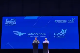 Photo of a presentation between President of Oman's CAA and AeroAsia's CEO (right to left) with a large board behind titled "GMF AeroAsia Garuda Indonesia Group".
