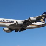 A Singapore Airlines Airbus A380-841 in the air, against a clear blue sky.