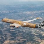An aerial shot of the A350F from the air depicting the sandy brown freighter making its maiden flight. The sky is crystal clear with the ground being visible from behind the aircraft.