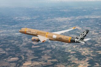 An aerial shot of the A350F from the air depicting the sandy brown freighter making its maiden flight. The sky is crystal clear with the ground being visible from behind the aircraft.
