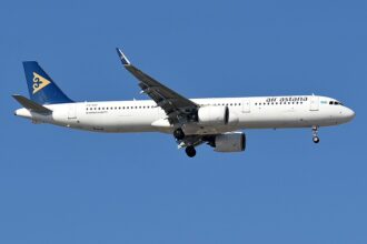 Air Astana Airbus A321neo in flight against a clear blue sky, landing gear down, with a white fuselage and a blue tail bearing a gold emblem.