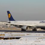 A wintery day featuring a Lufthansa Airbus A330-343X on the runway in Frankfurt Airport. The ground is white with lightly dusted snow and the classic Lufthansa colours of white, yellow and navy can be seen.