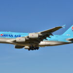 A aircraft with blue fuselage flying against a blue, clear sky