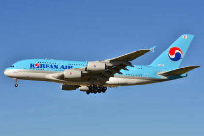 A aircraft with blue fuselage flying against a blue, clear sky
