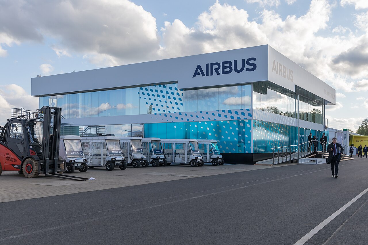 Airbus building in Schönefeld, Germany, featuring a big modern architecture with turquoise windows and a white exterior with the Airbus logo presented in a deep blue shade. Taken during an Air Show in 2018.