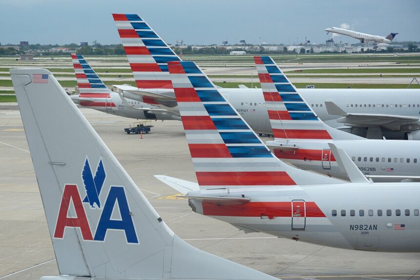 American Airlines aircraft at O'Hare that are parked side-by-side causing the brightly coloured aircraft tails to overlap each other. An aircraft is taking off in the distance into a clear sky.