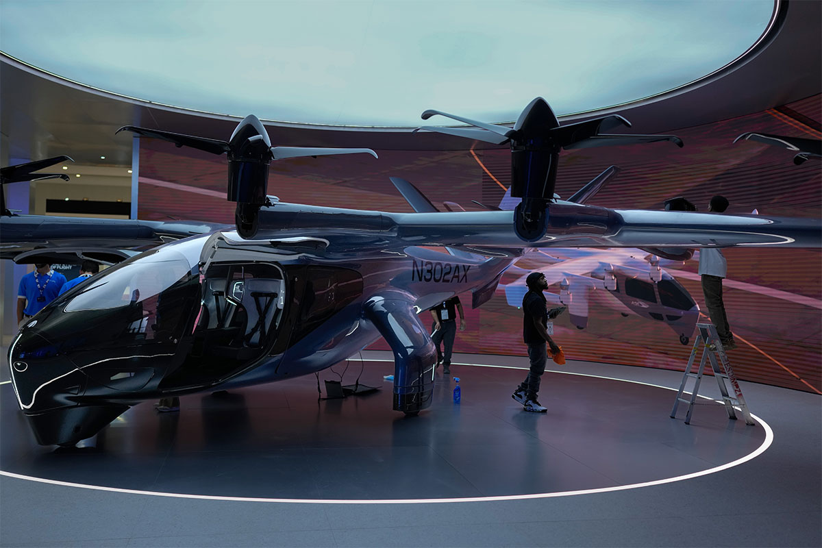 A sleek, dark blue electric vertical takeoff and landing aircraft with registration N302AX sits in a circular, modern showroom with people nearby.