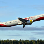 An Avolon Airbus A321-231 aircraft taking off of the runway. The livery on the aircraft is red and spells out 'Kings'. The sky is bright blue and clear in the background.